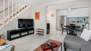 Ein modernes Wohnzimmer mit Flachbildfernseher, einer Couch, einem Couchtisch mit einem Schachspiel und einer Treppe.