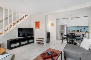 Ein modernes Wohnzimmer mit Flachbildfernseher, einer Couch, einem Couchtisch mit einem Schachspiel und einer Treppe.