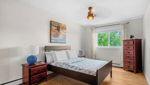 Ein Schlafzimmer mit Bett, Nachttischen, einem Schminktisch, einem Fenster mit Vorhängen und einer Deckenleuchte.