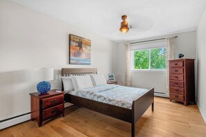 Ein Schlafzimmer mit Bett, Nachttischen, einem Schminktisch, einem Fenster mit Vorhängen und einer Deckenleuchte.