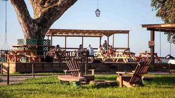 Ein Sitzbereich im Freien mit Holztischen und -stühlen, einem großen Baum und einer Pergola aus Holz.
