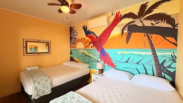 Ein Hotelzimmer mit zwei Betten, einem Deckenventilator, einem Gemälde mit tropischer Szenerie und einer Klimaanlage.