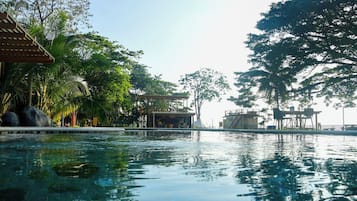 Ein Schwimmbad mit Holzterrasse, umgeben von üppiger Vegetation und einem Pavillon.
