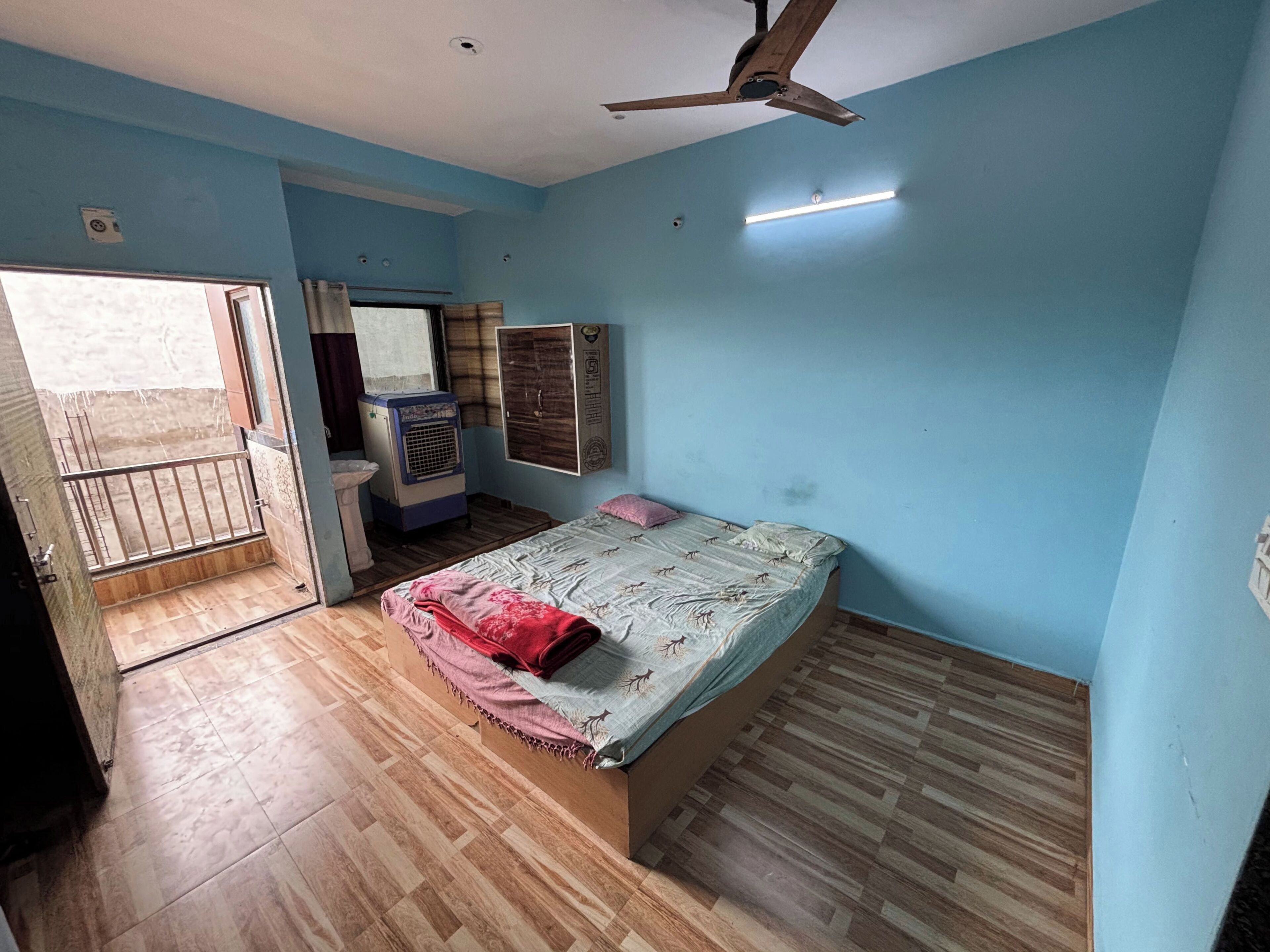 Un dormitorio con cama, ventilador de techo, ventana, armario y radiador.