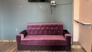 A room with a purple sofa, a mounted television, and a wooden floor. - MANAN PALACE HOTEL (Mungaoli)