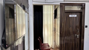 A room with a wooden door labeled 'TOILET,' a red plastic chair, and a partially open door leading to another room. - MANAN PALACE HOTEL (Mungaoli)
