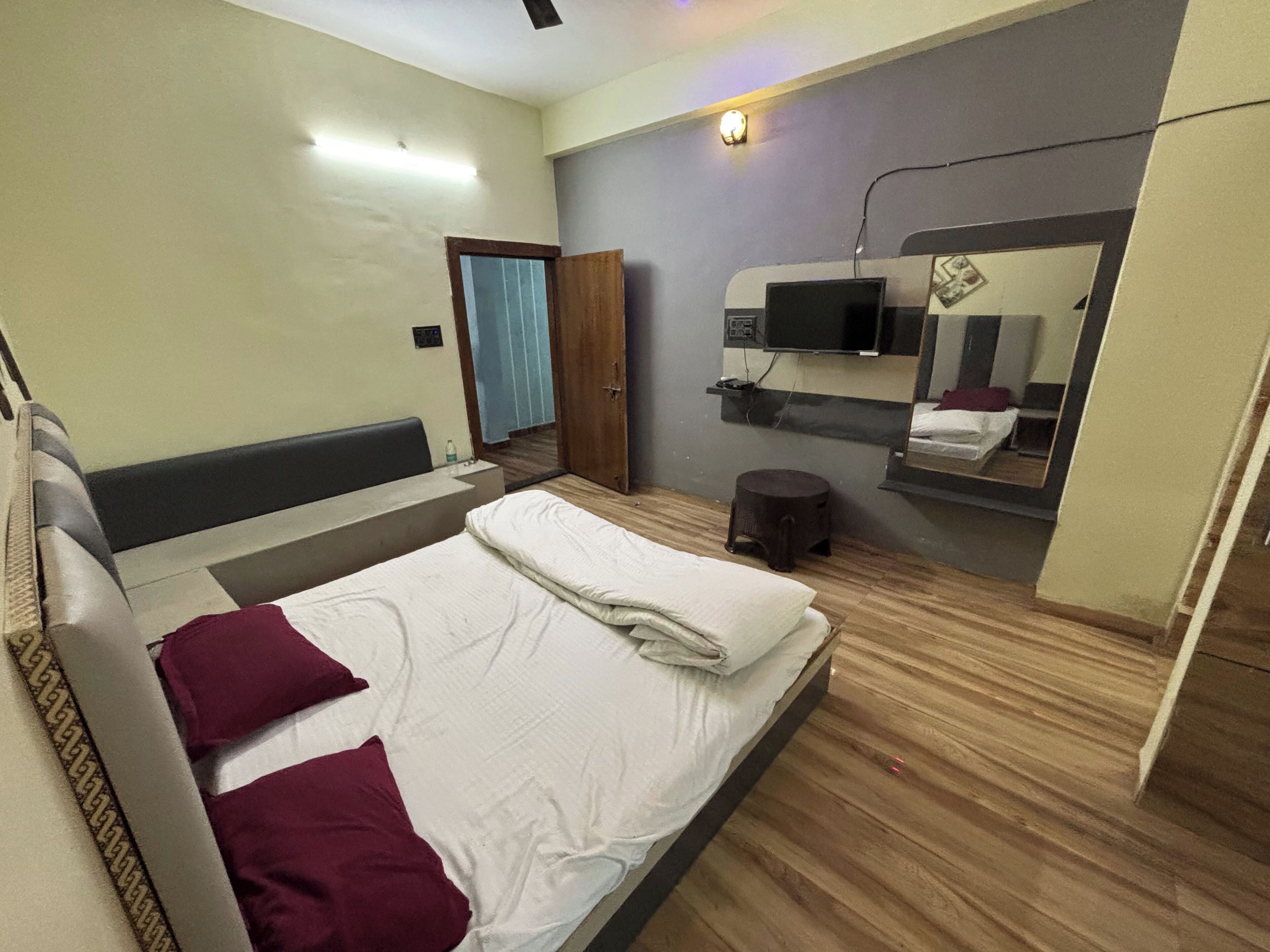 Une chambre à coucher avec un lit, un petit tabouret, une télévision et un miroir.