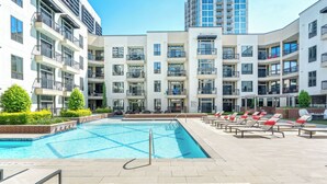 Un moderno complejo de apartamentos con piscina, mobiliario exterior y un edificio alto al fondo.