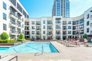 A modern apartment complex with a swimming pool, outdoor seating, and a tall building in the background. - Executive 1BR Houston Balcony, Fast Wi-Fi and In-Unit Laundry (Houston)