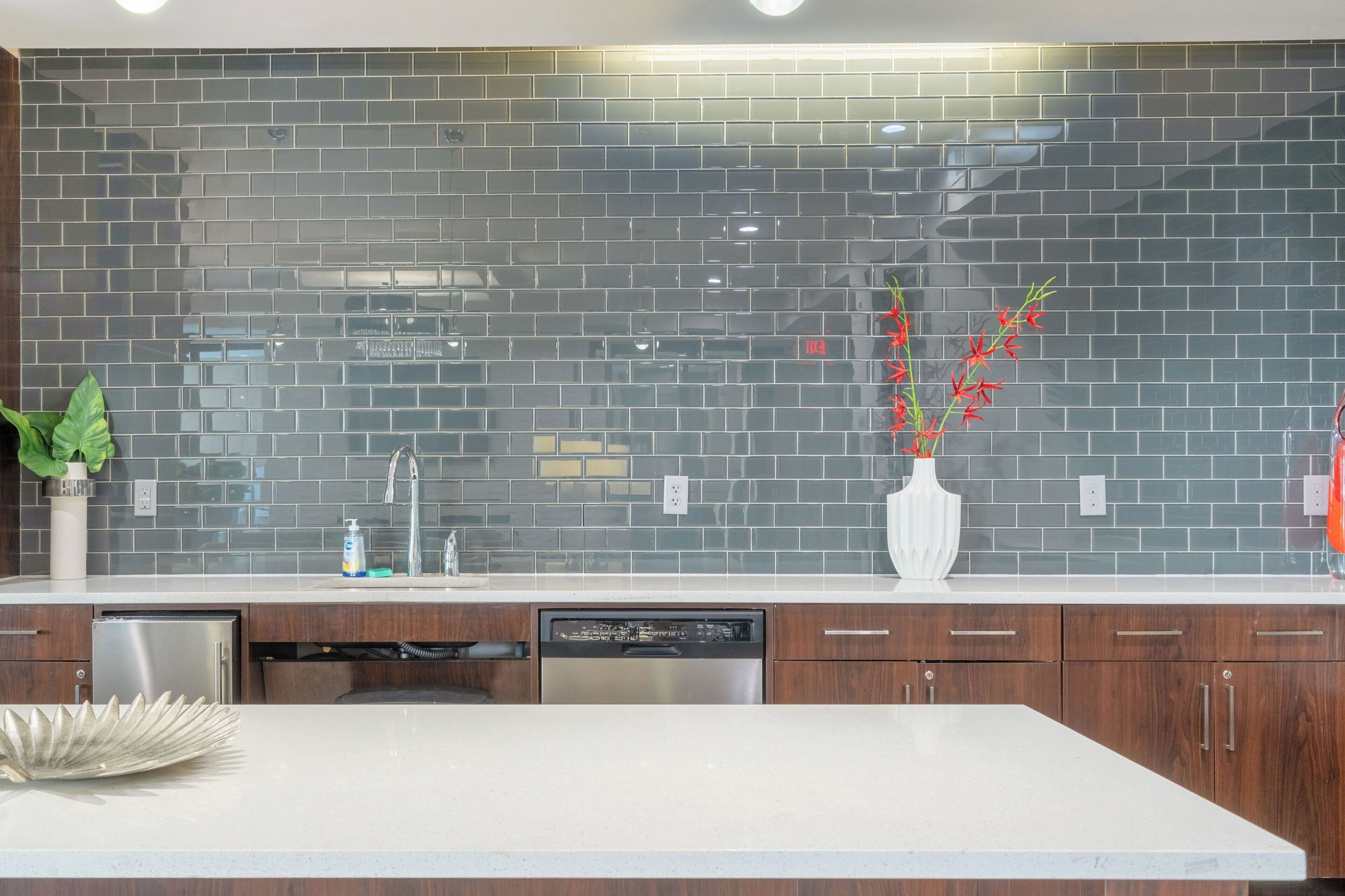 A modern kitchen with a black tiled backsplash, stainless steel appliances, and wooden cabinets.