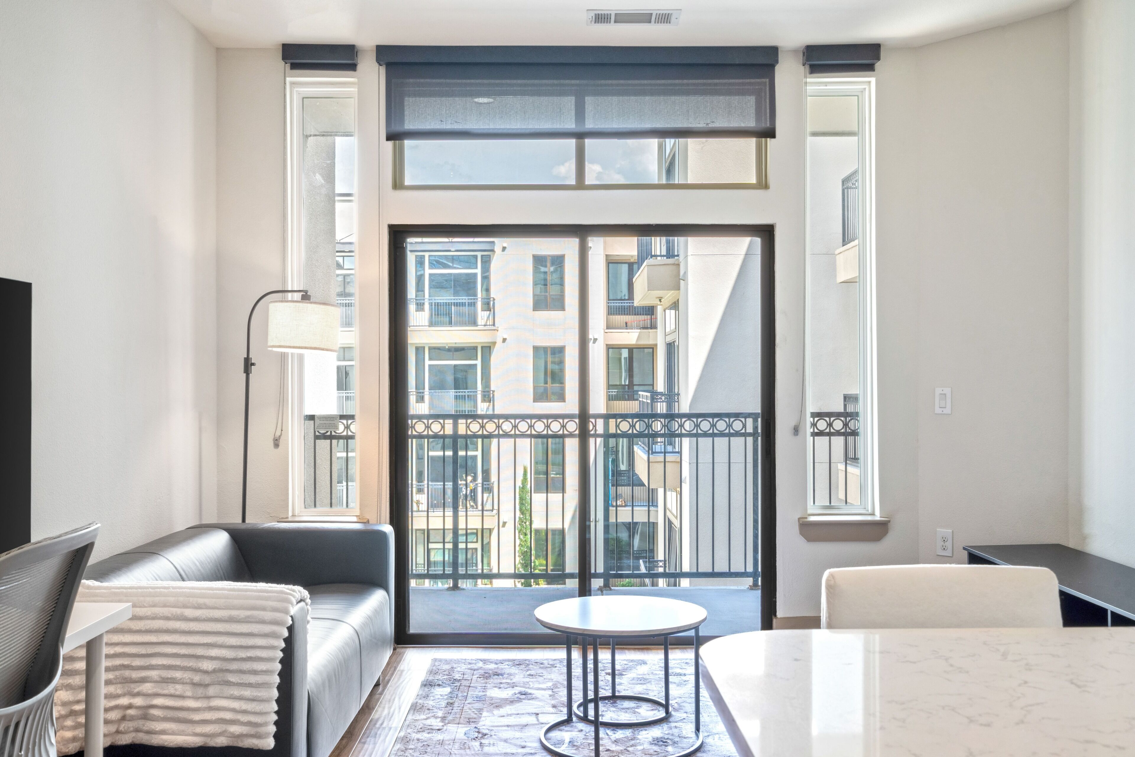 A modern living room with a sofa, a coffee table, and a view of a building through large windows.