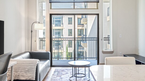 Una sala de estar moderna con un sofá, una mesa de centro y vistas a un edificio a través de amplios ventanales.