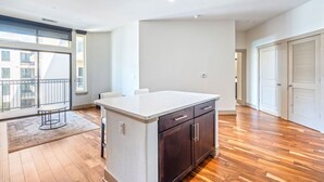 Amplia habitación con piso de madera, una isla de cocina con alacenas oscuras, un ventanal con balcón y una puerta con diseño persa.