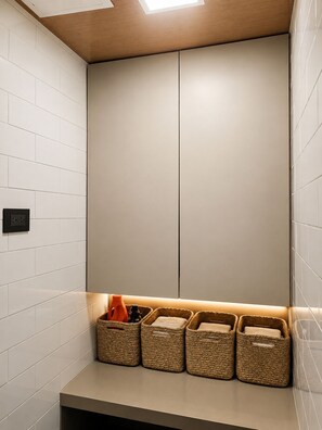 Ein Badezimmer mit weiß gefliesten Wänden, Holzboden und einer eingebauten Sitzbank mit Stauraumkörben.