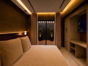 Ein modernes Schlafzimmer mit einem großen Bett, einem Nachttisch, einem Fernseher und Blick ins Freie durch eine Schiebetür.