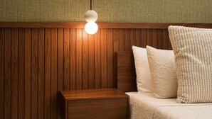 A wooden bedside table with a drawer, a bed with a white quilted bedspread and pillows, and a wall with vertical wooden panels. - Modern 1BR Retreat with Private Jacuzzi & Patio up to, 4 guests allowed. (Santiago De Los Caballeros)