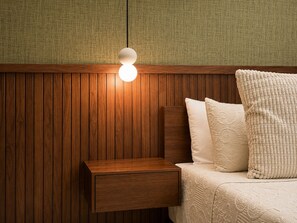 A wooden bedside table with a drawer, a bed with a white quilted bedspread and pillows, and a wall with vertical wooden panels. - Modern 1BR Retreat with Private Jacuzzi & Patio up to, 4 guests allowed. (Santiago De Los Caballeros)