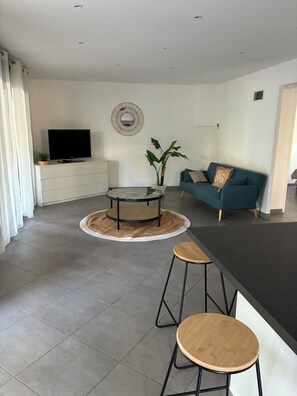Ein modernes Wohnzimmer mit Fernseher, Sofa und einem runden Tisch mit Hockern.