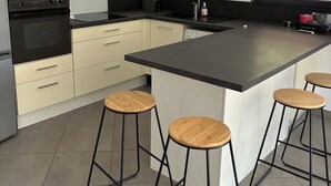 A modern kitchen with a central island, bar stools, a microwave, and a stove. - TO THE SOUND OF BIRDSONG House in Provence with private garden and parking (Les Pennes-Mirabeau)
