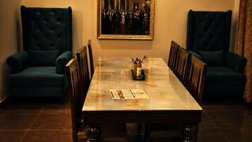 A dining room with a marble table, upholstered chairs, a chandelier, and a painting on the wall.
