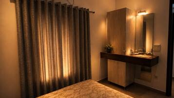 A bedroom with a bed, a vanity with a mirror, and an air conditioning unit on the wall.