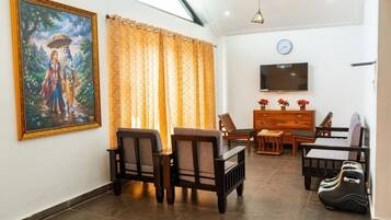 A living room with a TV, wooden furniture, a painting, and curtains.