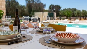 Un tavolo da pranzo apparecchiato con bicchieri da vino, piatti e posate, con vista su una piscina e alberi.
