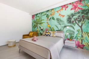 A bedroom with a bed, a nightstand, a small stool, and a wall with a tropical mural. - Trullo Elisa by Perle di Puglia (Carovigno)