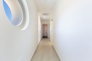 A narrow hallway with a circular window on the left, a door at the end, and a ceiling vent. - Trullo Elisa by Perle di Puglia (Carovigno)