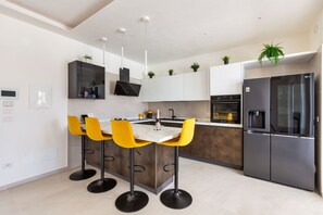 A modern kitchen with a central island, bar stools, a built-in oven, and a refrigerator. - Trullo Elisa by Perle di Puglia (Carovigno)