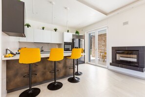 A modern kitchen with three yellow bar stools, a built-in oven, and a fireplace. - Trullo Elisa by Perle di Puglia (Carovigno)