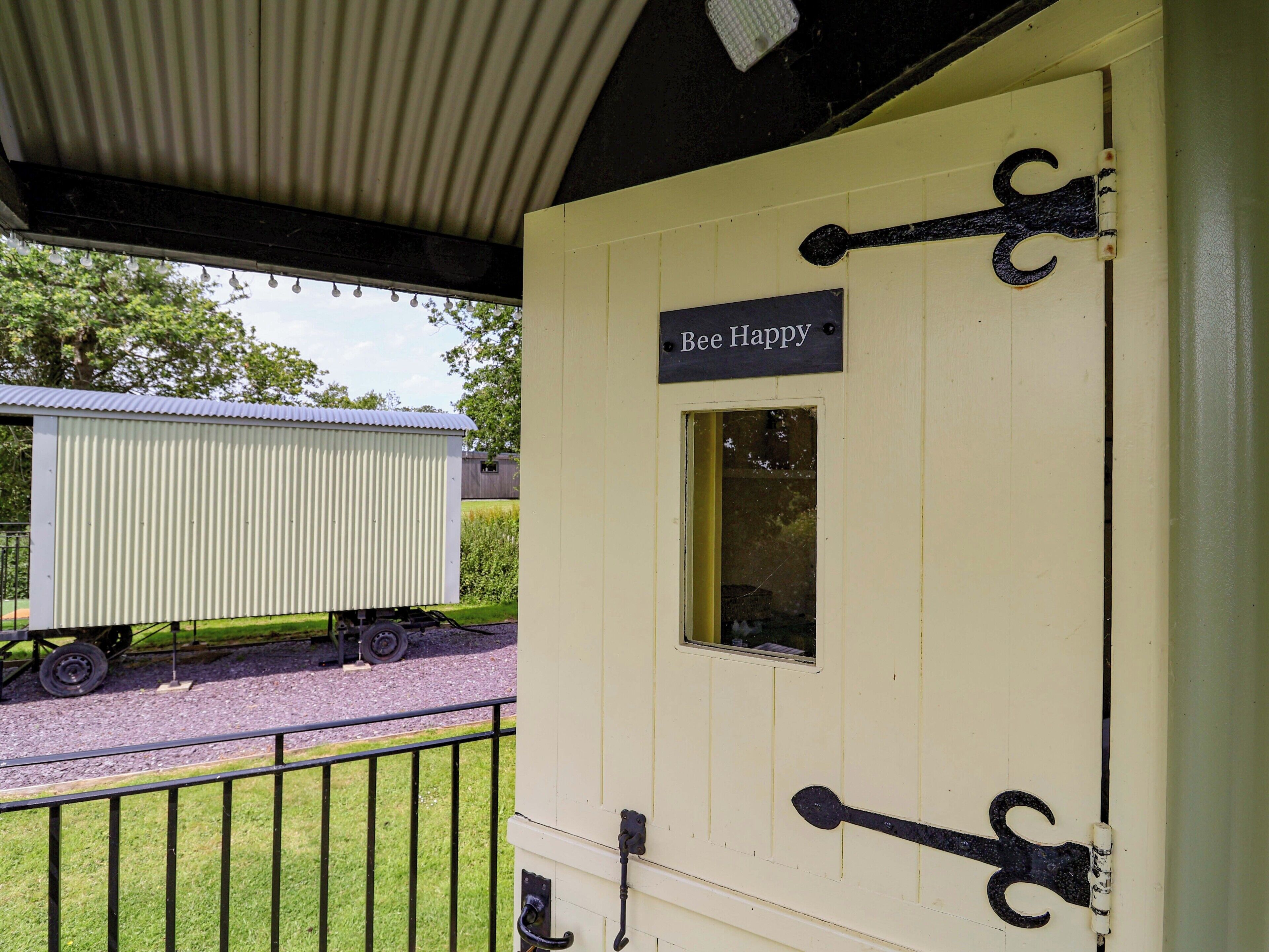 A yellow door with a sign reading 'Bee Happy,' a window, and a metal handle.