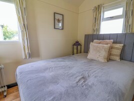 Un dormitorio con cama, un cuadro en la pared, una ventana con cortinas y una mesita de noche con lámpara.