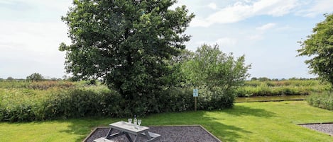A picnic table with a gravel base surrounded by grass and trees.
