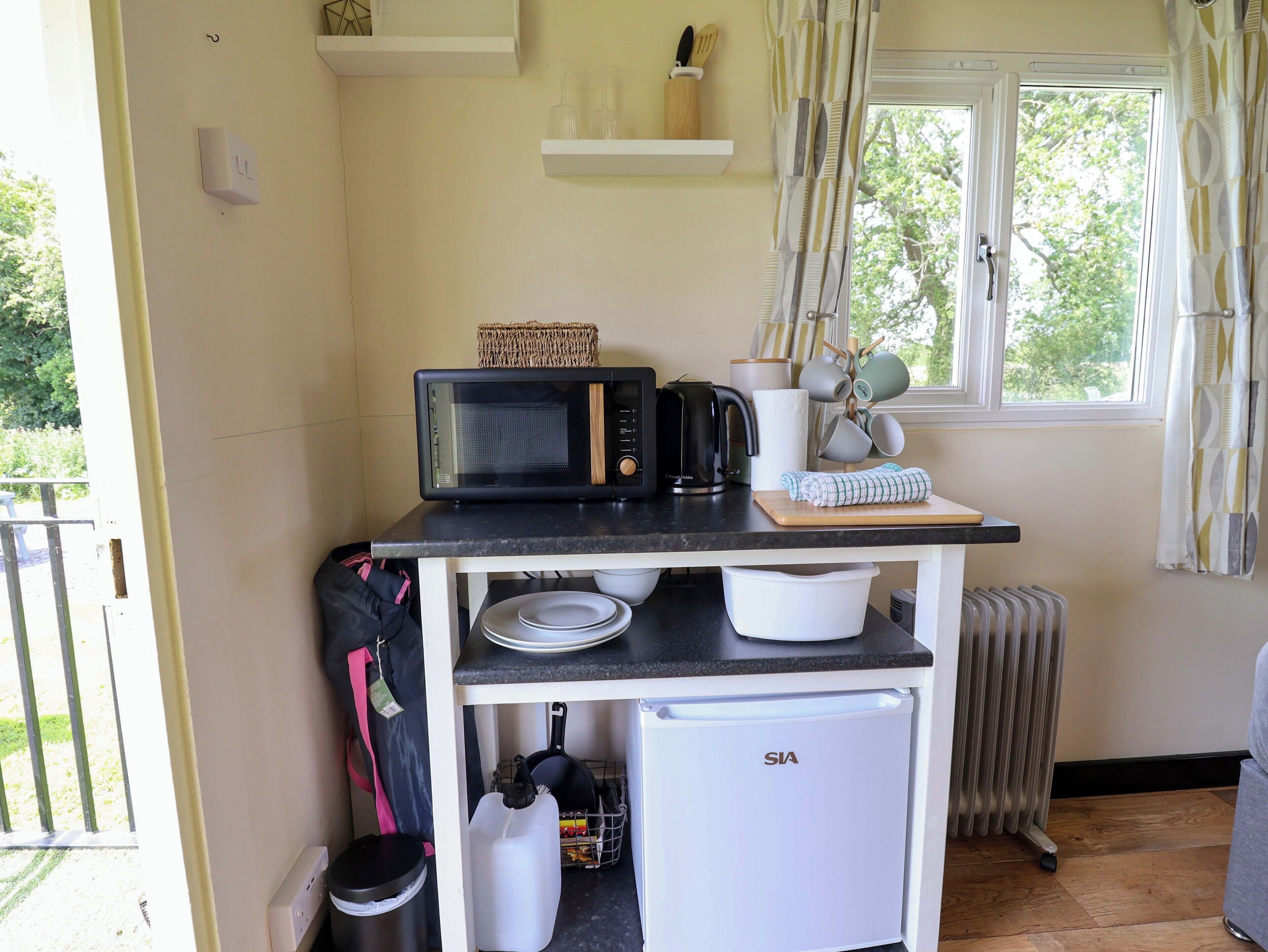 Una kitchenette compacta con microondas, hervidor y un refrigerador pequeño.