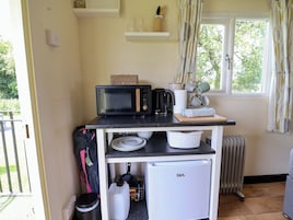 Una kitchenette compacta con microondas, hervidor y un refrigerador pequeño.