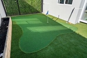 A well-maintained artificial green turf golf putting area with a flagstick, surrounded by a wooden fence and a hedge. - Sangrove Residence - Four Bedroom House, Sleeps 8 (Cape Town)