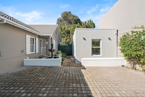 A paved courtyard with a fountain, a white building with a window, and a tree. - Sangrove Residence - Four Bedroom House, Sleeps 8 (Cape Town)