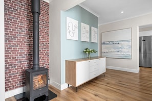 A modern living room with a brick wall, a black wood-burning stove, a white cabinet, and artwork on the wall. - Sangrove Residence - Four Bedroom House, Sleeps 8 (Cape Town)