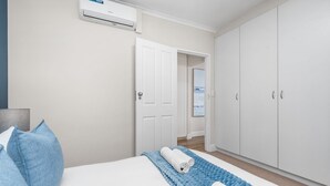 Una camera da letto con un letto, una coperta blu, asciugamani bianchi, un armadio e un condizionatore d'aria.