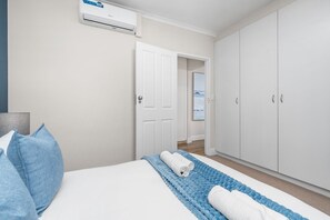 A bedroom with a bed, a blue blanket, white towels, a wardrobe, and an air conditioning unit. - Sangrove Residence - Four Bedroom House, Sleeps 8 (Cape Town)