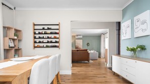 Un'area pranzo moderna con un tavolo e sedie in legno, una dispensa per vini con bottiglie, e vista su un soggiorno con un divano.