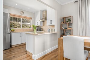 Una cocina moderna con armarios blancos, una isla central, estufa integrada y una ventana con vistas al verdor.