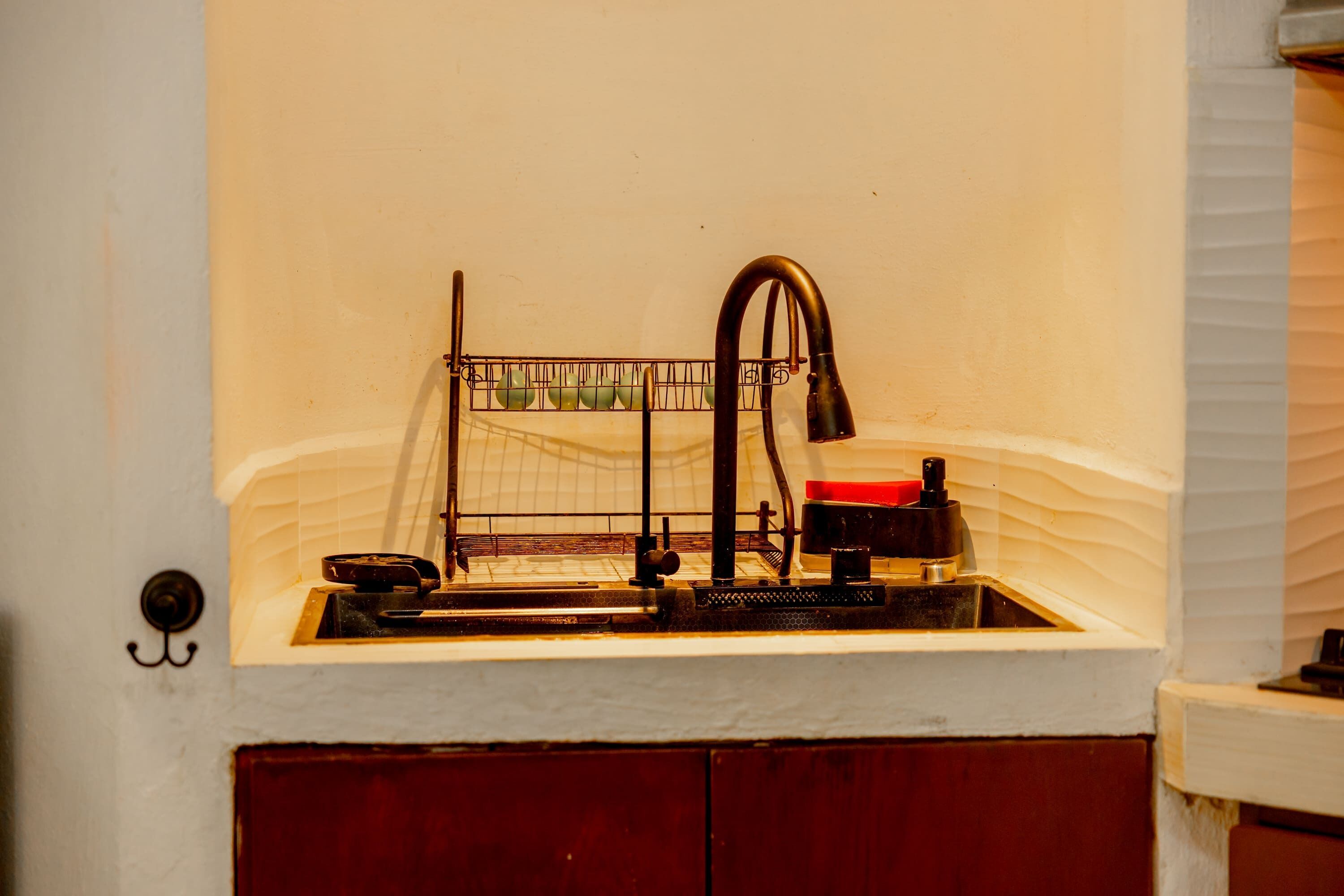A kitchen with a sink, a fruit basket, and a red container.