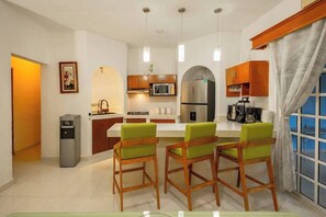 A modern kitchen with a central island, wooden chairs, a refrigerator, a microwave, and a coffee maker. - Spacious House | 4 BR | Pool, Gym & Terrace (Mérida)