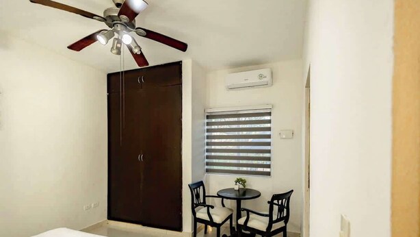 A bedroom with a bed, a wardrobe, a ceiling fan, a window with blinds, and a small table with two chairs. - Spacious House | 4 BR | Pool, Gym & Terrace (Mérida)