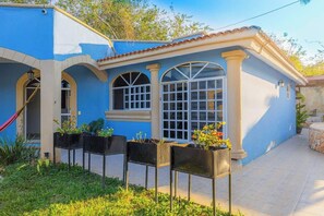 Ein blaues Haus mit einem Ziegeldach, einer überdachten Terrasse und einem Garten mit Pflanzkästen.