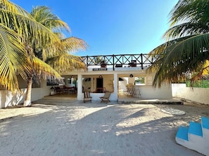 Une villa située en bord de mer, dotée d’un patio couvert, de palmiers et surplombant un ciel d’un bleu limpide.