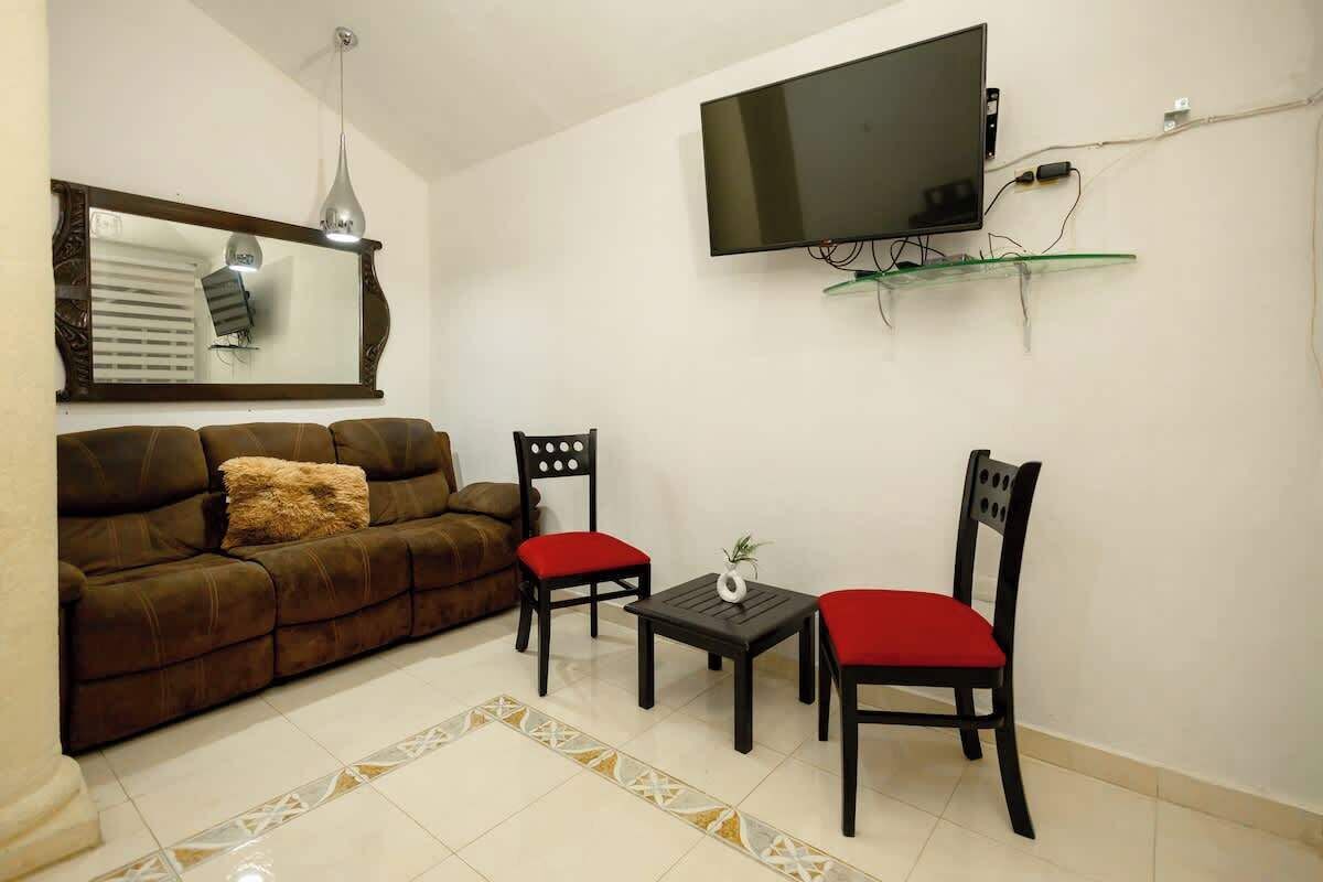Un salon comprenant un canapé, deux fauteuils, une table basse, un téléviseur à écran plat fixé au mur et un miroir décoratif.