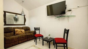 Un salon comprenant un canapé, deux fauteuils, une table basse, un téléviseur à écran plat fixé au mur et un miroir décoratif.